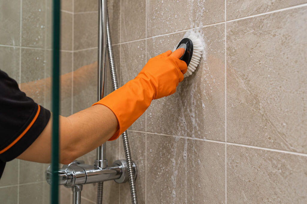 Cleaner scrubbing bathroom tiles and grout during a deep clean